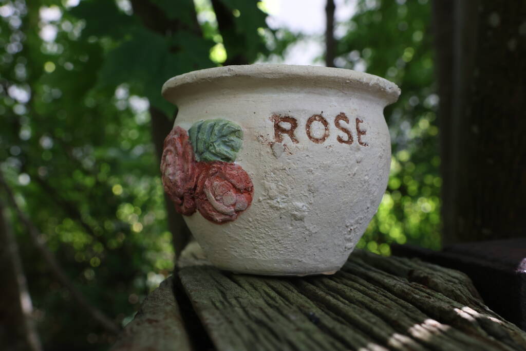 A forgotten ceramic mug with a rose and name ROSE on it, standing on a wooden buffer stop.