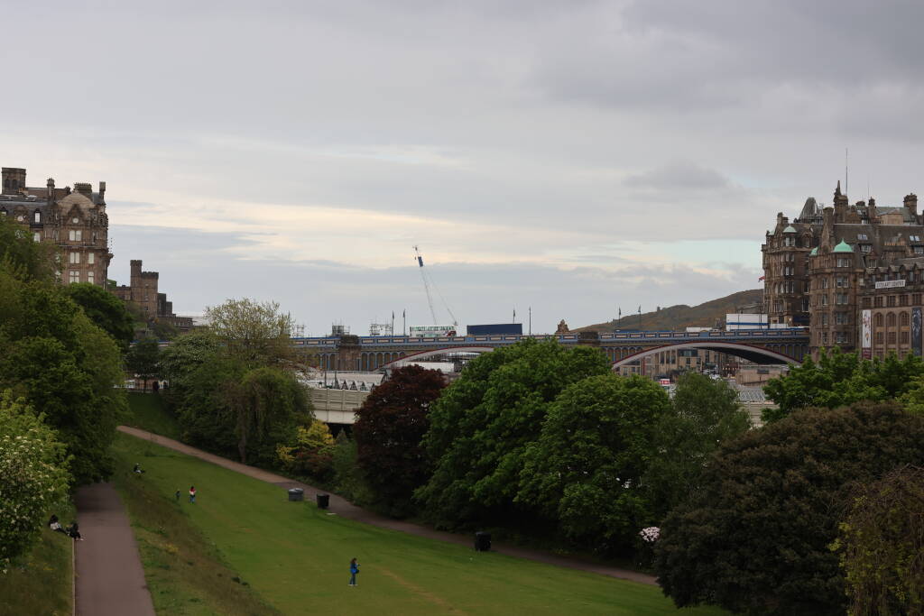 A park nearby the railway station. Tracks to the right behind trees, white roofs in the middle are of Waverlay train station, North Bridge in background.