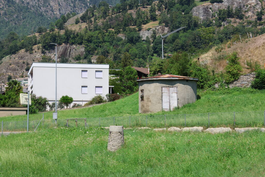 An unassuming round building and a little item (how would you call the round thing in foreground?) were vital to precisely measure the position of Simplon tunnel at the beginning of the 20th century. The tunnel portal is at the other bank of Rhôna.