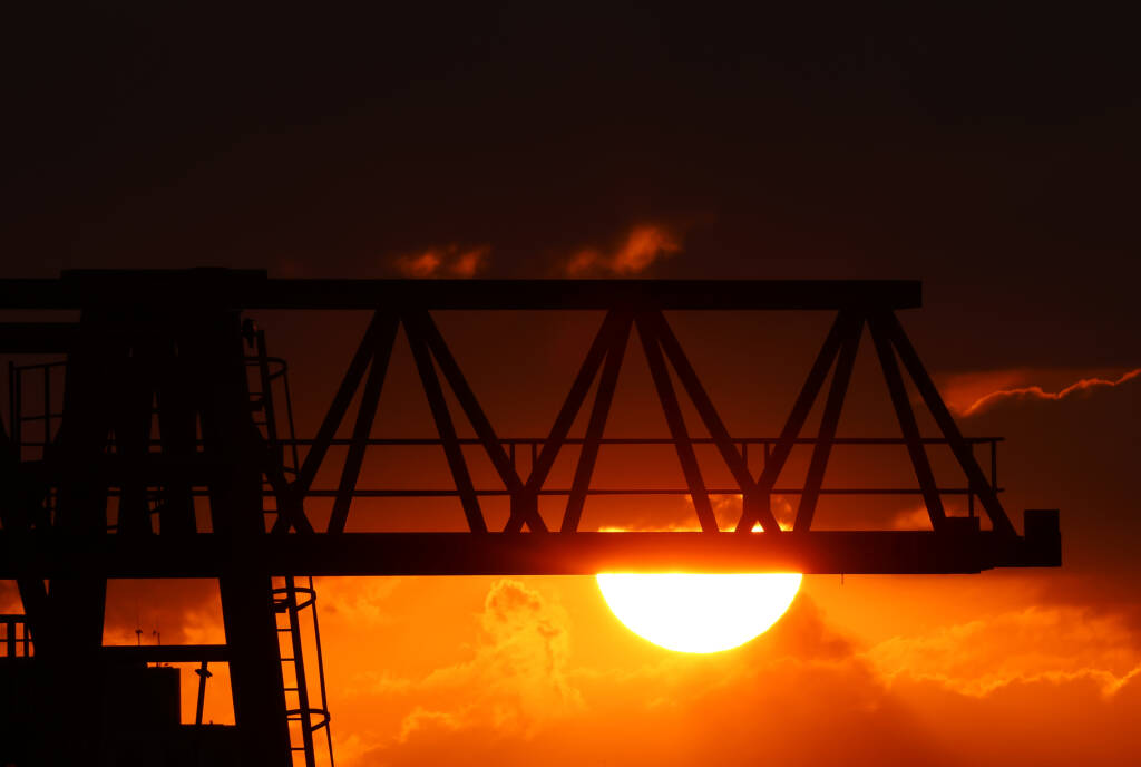 Setting sun behind a cloud and a gantry crane.